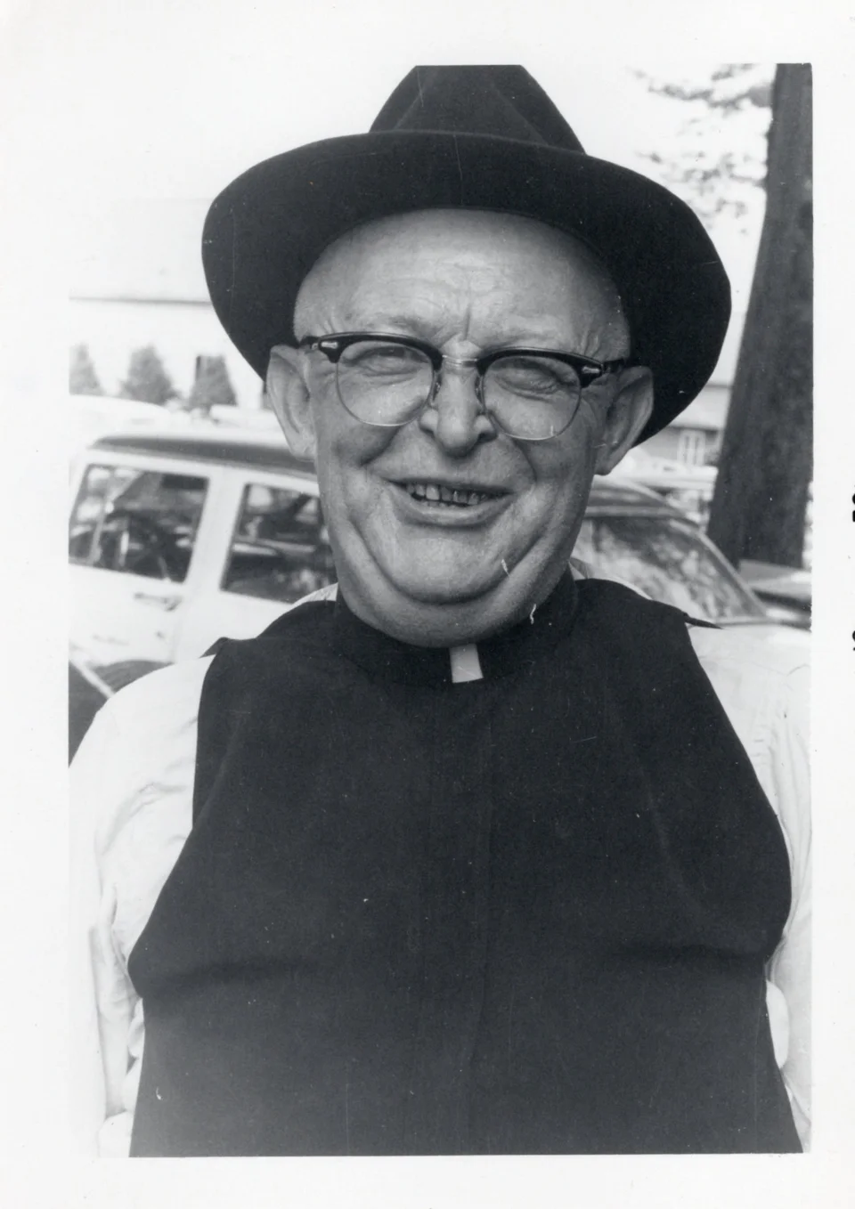 Father George John Niekamp smiling outdoors in a hat and clerical clothing